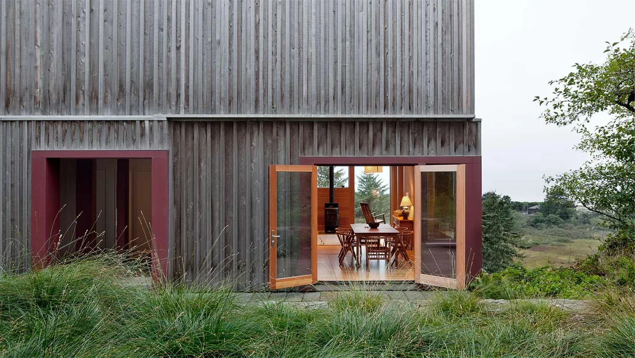 The Neskowin Beach House features vertical wooden siding and folding glass doors opening to a dining room.