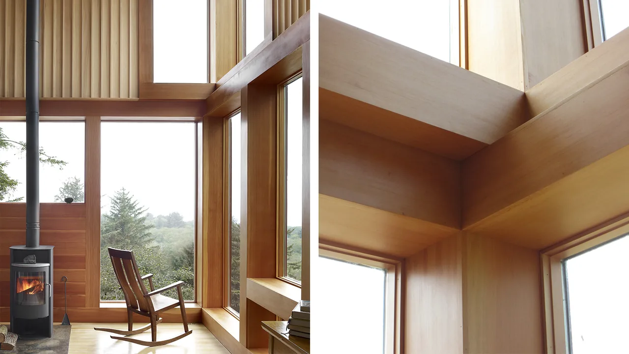 Wood-paneled interior with floor-to-ceiling windows and a wood-burning stove at the corner of the living space.