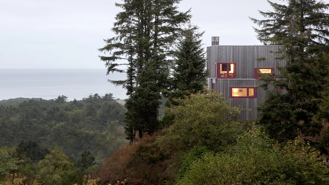 Neskowin Beach House with natural wood siding nestled in forested hillside, offering views of the ocean beyond.