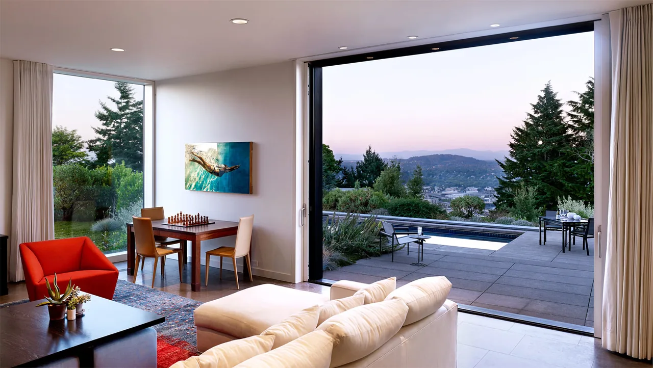 The Portland Heights Residence features a living room with expansive sliding glass doors opening to an outdoor patio overlooking a scenic city view.