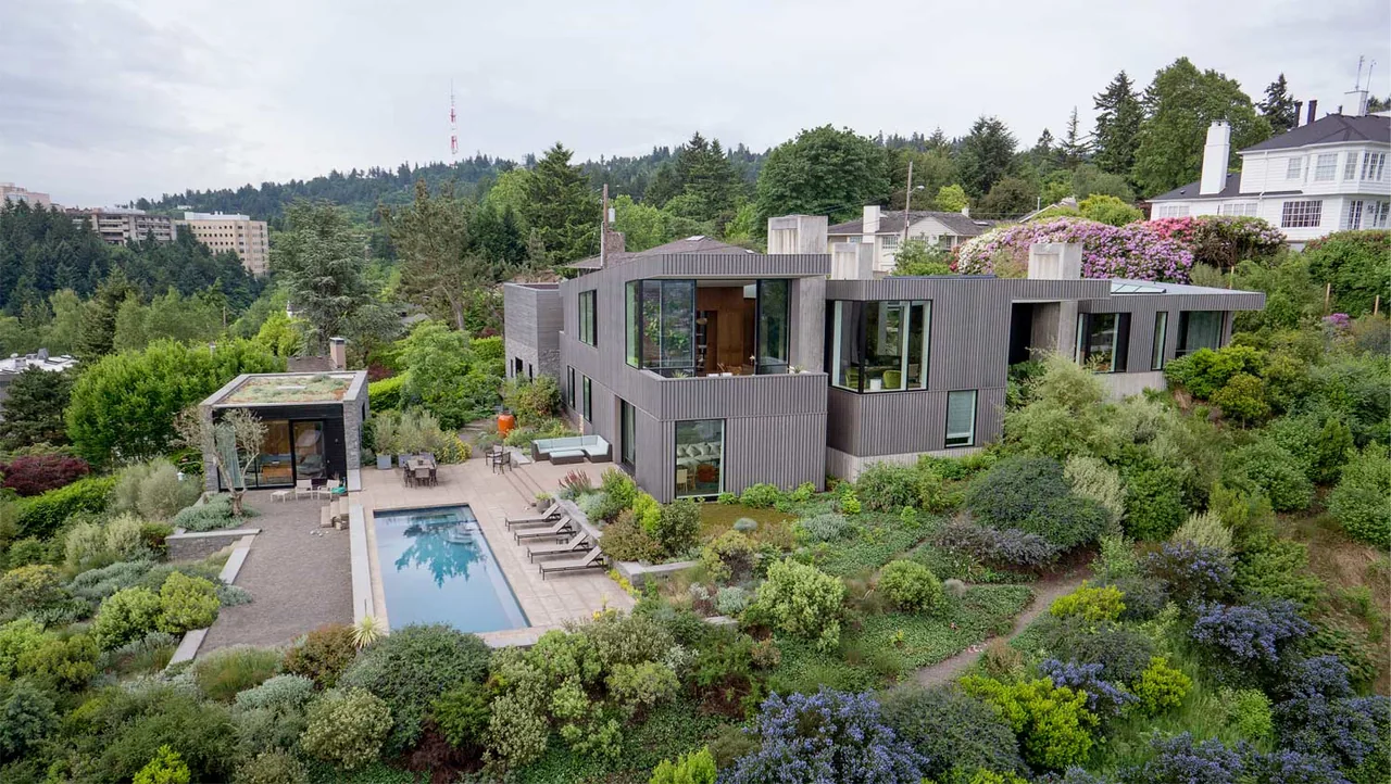 Portland Heights Residence features vertical wood siding and a pool nestled in dense greenery on a hillside lot.