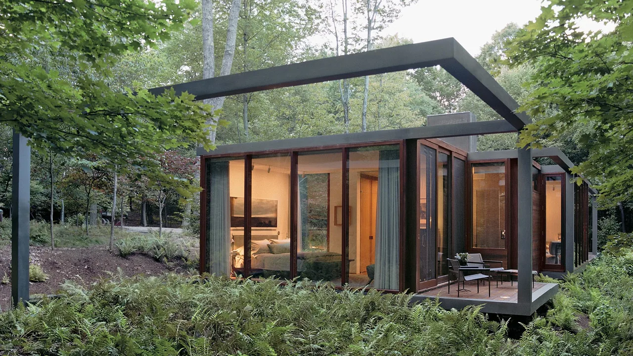 The Dutchess County Residence Guest House features a glass and metal frame exterior amid woodland vegetation.