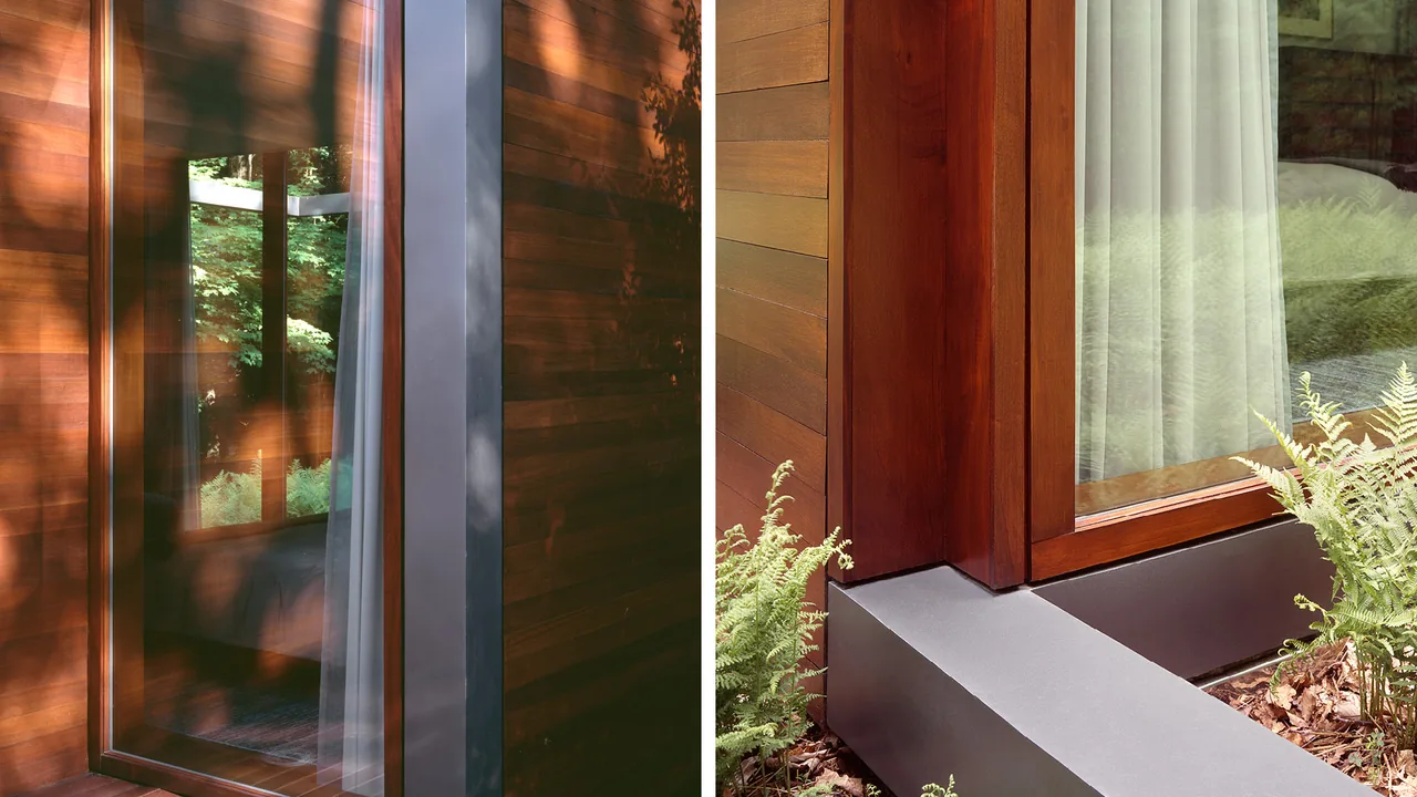 Detail of wooden window frames and vertical wood siding in a forest setting with garden ferns outside the guest house.