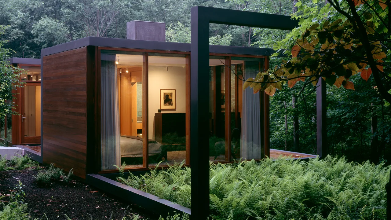 Guest house bedroom with floor-to-ceiling wooden framed glass walls overlooking a fern garden in a forest landscape.