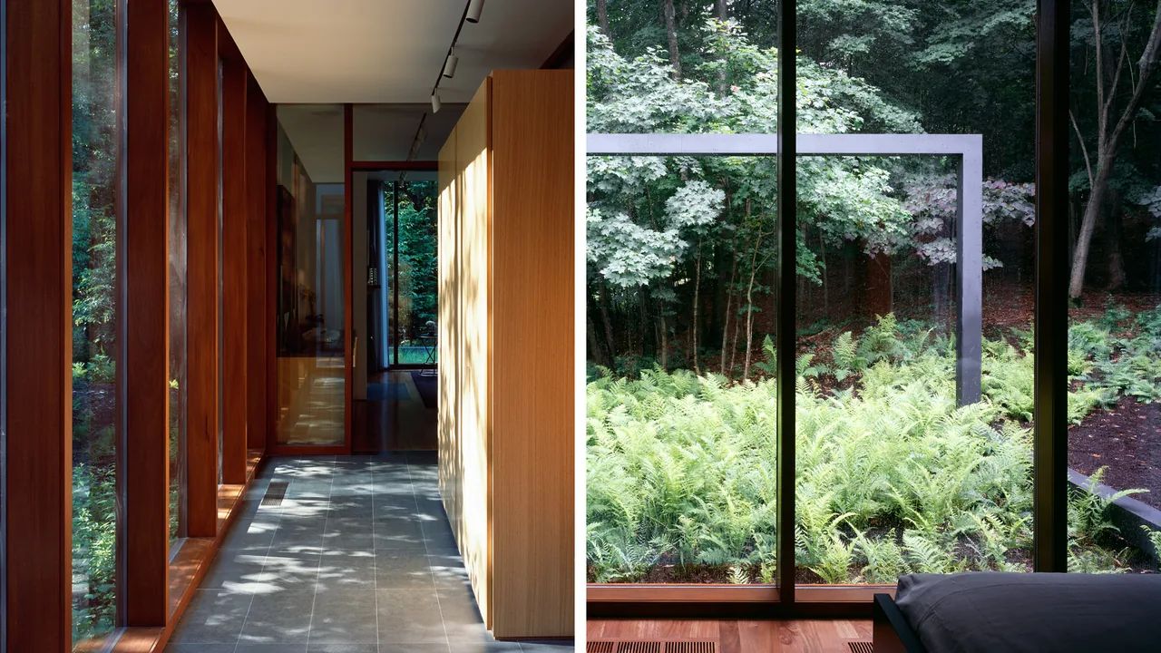 Corridor with large wood window frames and tile floor leads to glass door with view of forest and garden ferns outside.