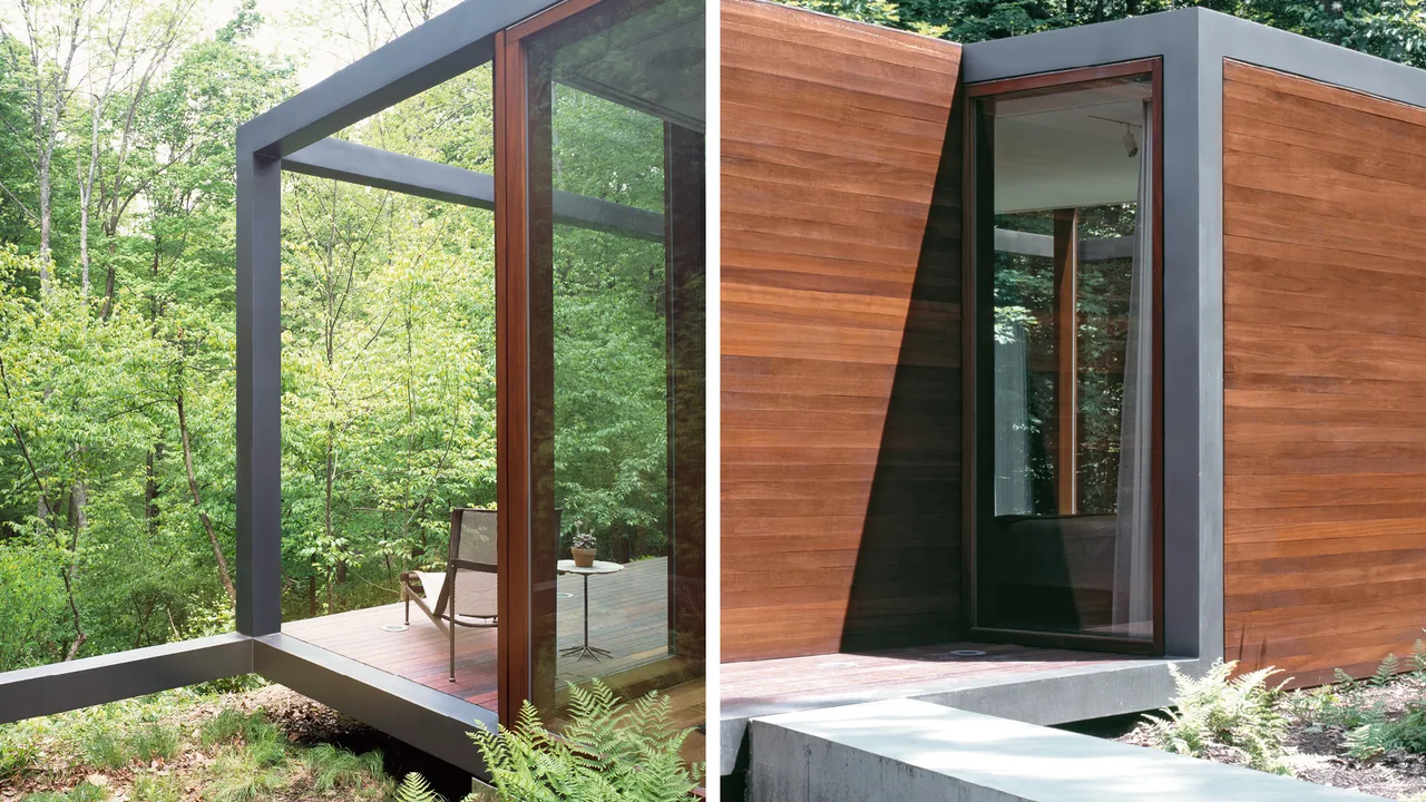 Modern guest house with rectangular wood siding, cantilevered patio, and large glass doors in a forest setting.