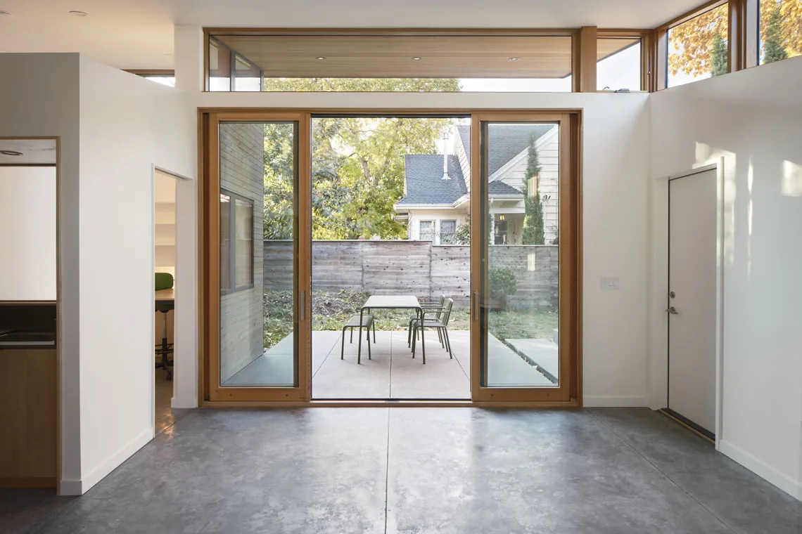 Room features large wood-framed sliding glass doors leading to a concrete patio with metal outdoor furniture and upper clerestory windows.