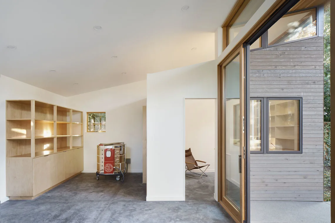 Studio: Portland showcases light wood built-in shelving and a concrete floor with a sliding glass door to an exterior with horizontal wood siding.
