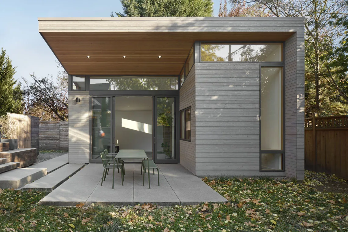 Modern exterior of Studio: Portland features horizontal wood siding, tall and small windows, and an overhanging roof above a patio.