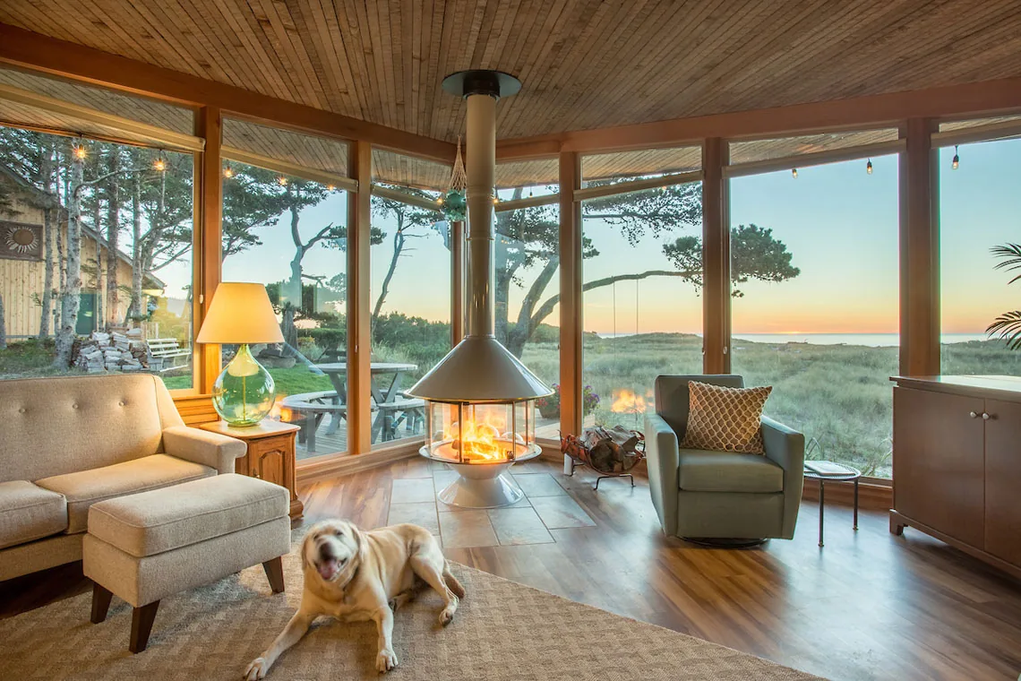 Living room with floor-to-ceiling windows and central freestanding hanging fireplace at sunset, part of Remodel: Oregon Coast project.