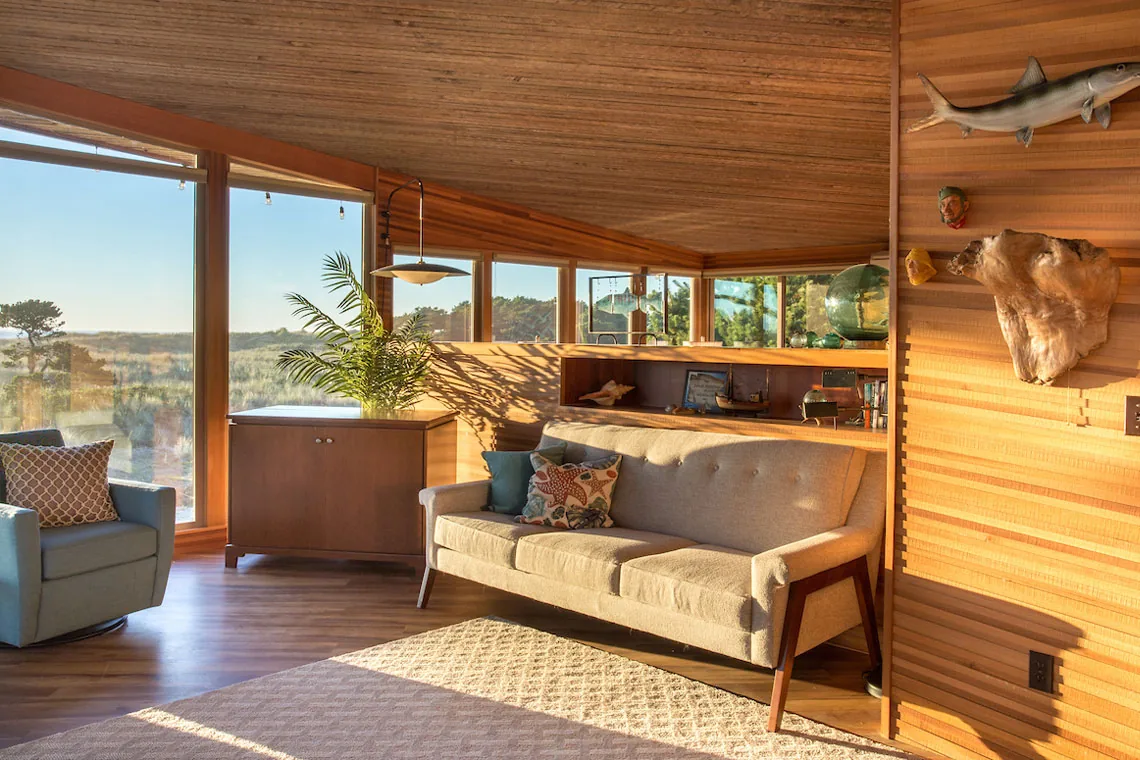 Living room features wood panel walls, a mid-century style sofa, an armchair, and large windows with landscape views.