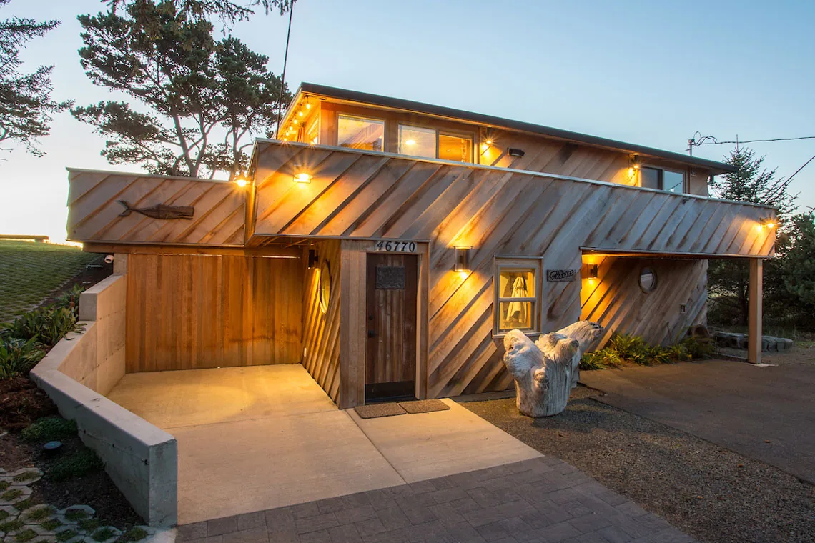 The Oregon Coast remodel by Webster Wilson Architect features a modern home with angled wood siding and warm exterior lighting.