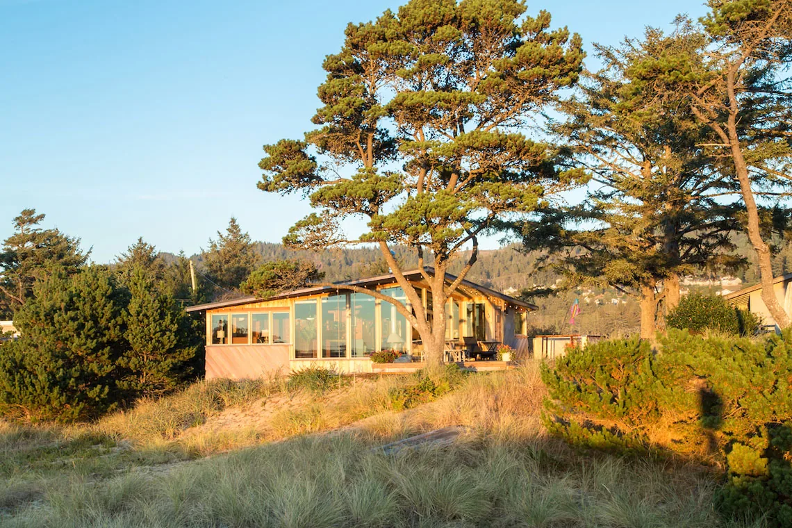 Coastal house with expansive floor-to-ceiling windows showcasing natural surroundings at sunset.