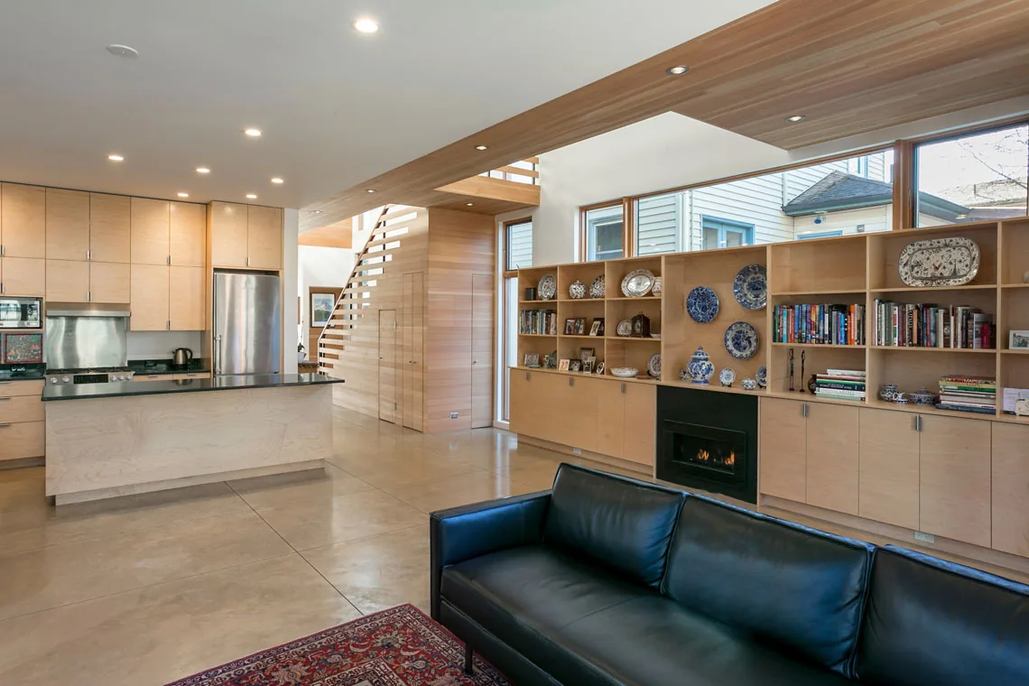 Open-plan living and kitchen space with built-in shelving, fireplace, and floating stair in a modern style home.