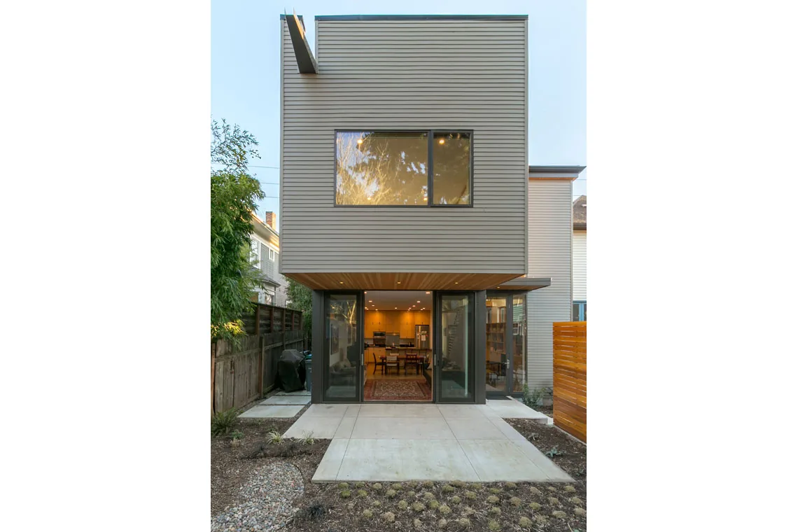 This Portland residence features a cantilevered upper floor with horizontal siding and floor-to-ceiling sliding glass doors on the lower level opening to a concrete patio.