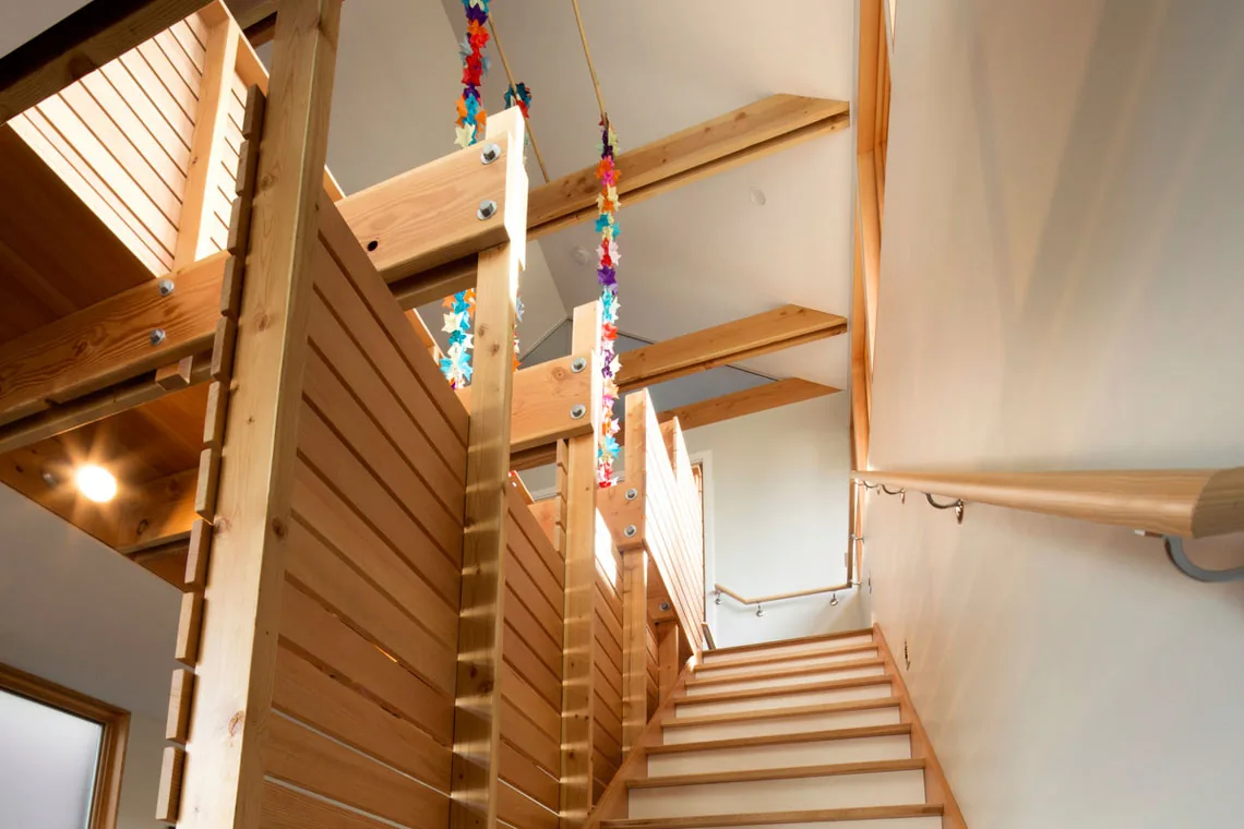 Stairwell with exposed wooden beams and slatted wood railing illuminated by recessed lights.