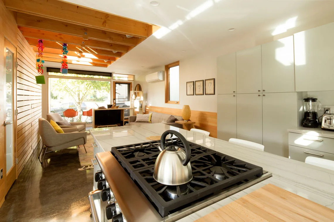 Interior view of an open kitchen and living area in ADU: Portland with wood detailing and appliances visible.