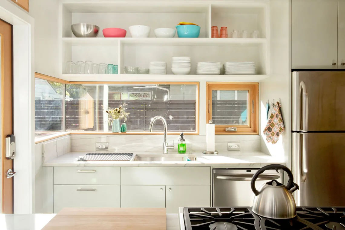 Kitchen with corner wood-framed windows, open white shelves, and stainless steel appliances.