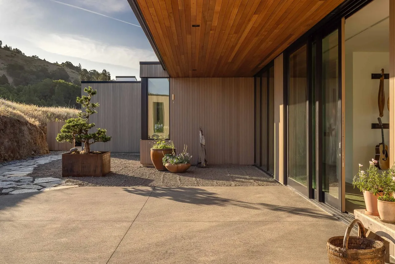 Modern residence patio with wood soffit and large glass sliding doors overlooks a natural hillside landscape.