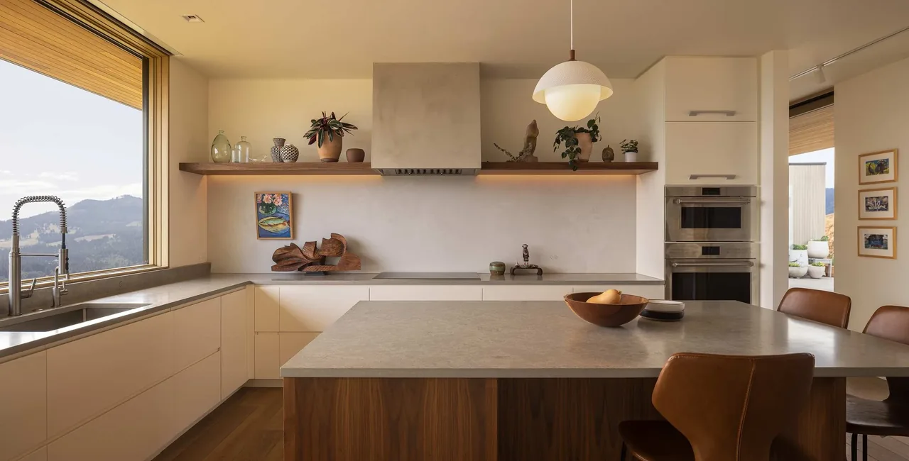 The kitchen in Bald Mountain Residence includes a large window with mountain views, a kitchen island, and minimalist cabinetry.