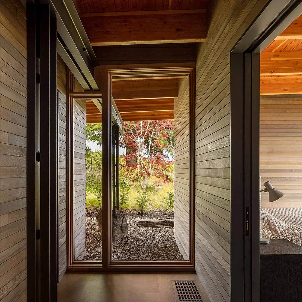 A wood-lined interior hallway with a floor-to-ceiling window looking out to a garden and colorful trees.