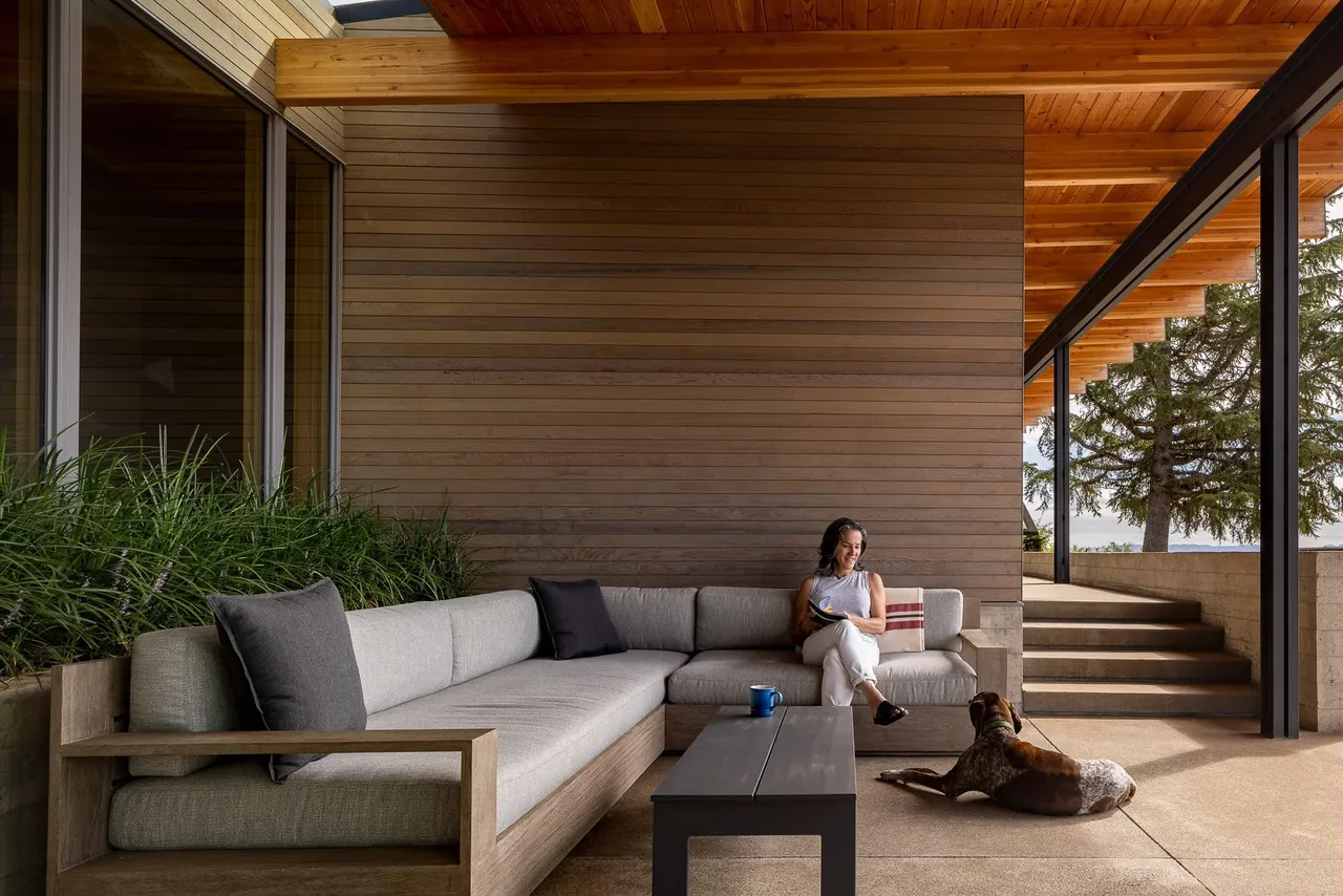 Covered patio with wood ceiling beams, built-in sectional sofa seating, and a concrete floor at Lone Feather Residence.