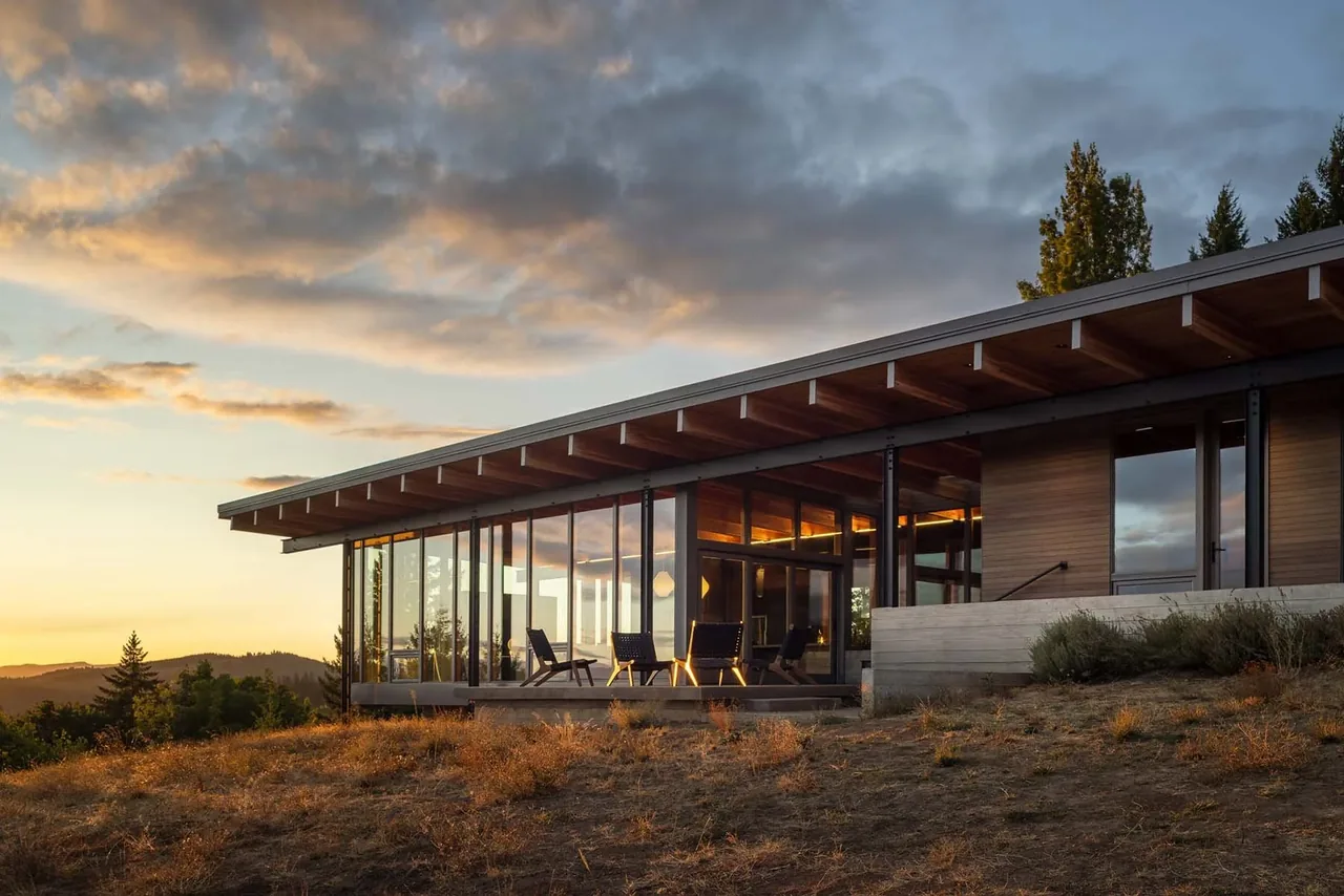 Lone Feather Residence features a flat roof, extensive glazing, and wood ceiling beams with panoramic forest views.
