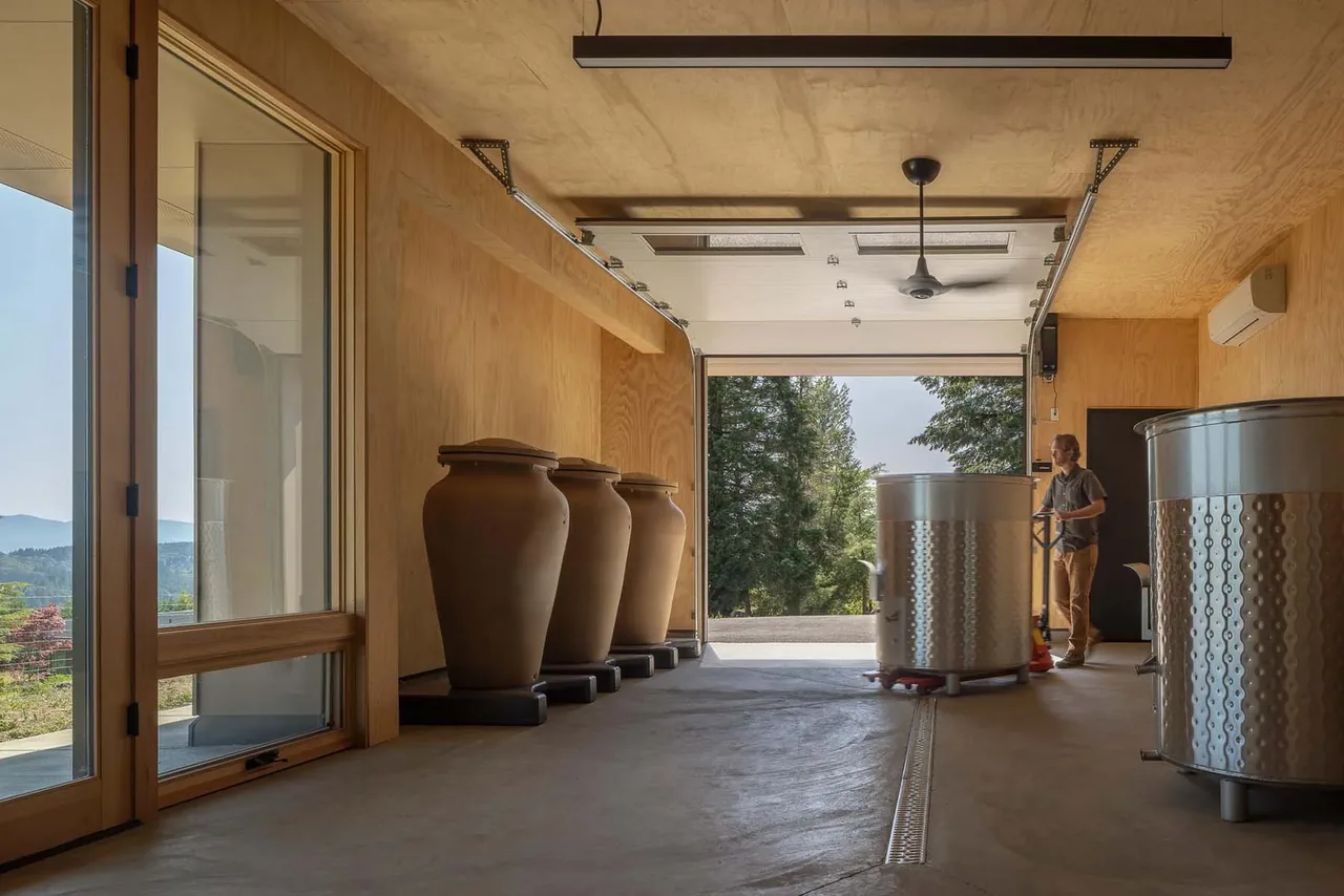 Garage space with wood panel walls and ceiling, featuring large urns and stainless steel tanks in a wood-paneled room with a view of trees.