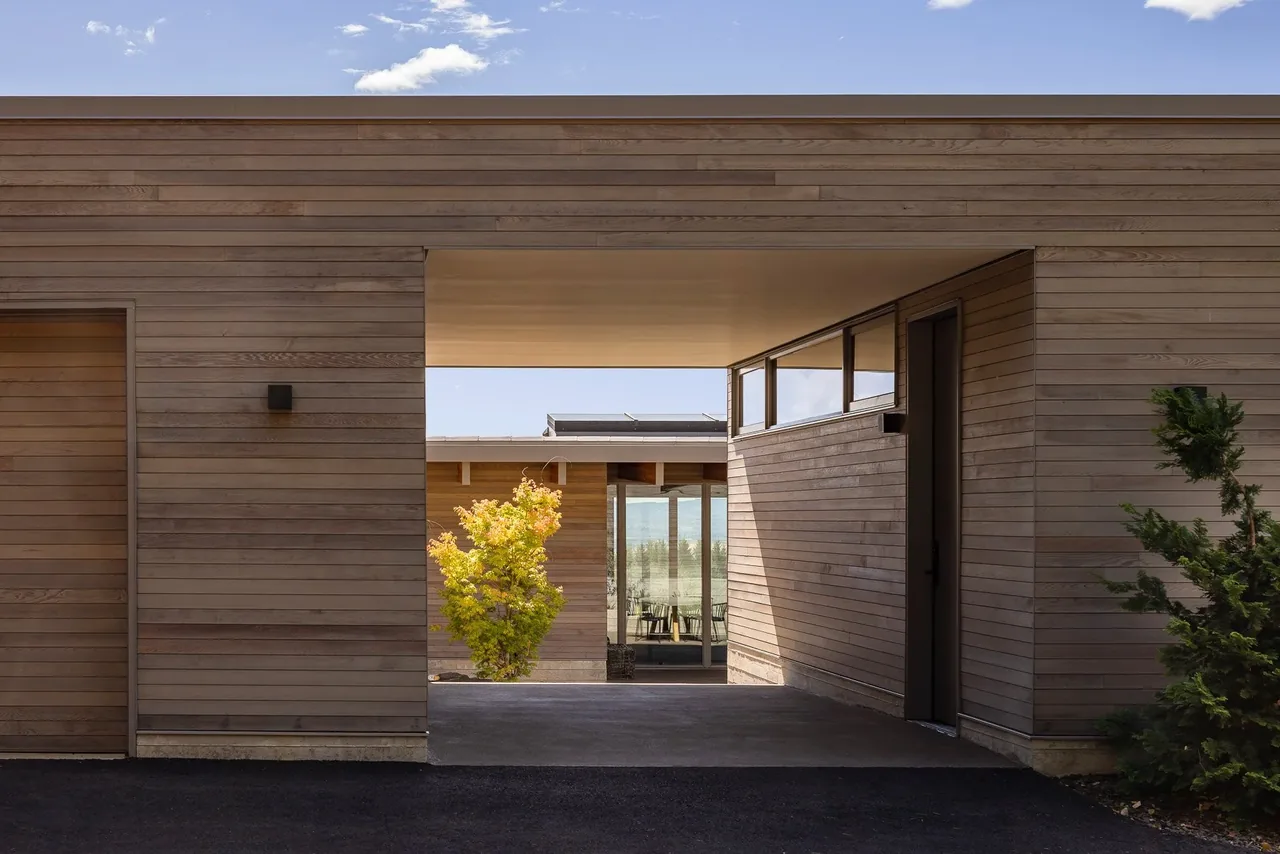 Lone Feather Residence features wood siding, an overhanging flat roof, and a passage view to a courtyard with glass walls.