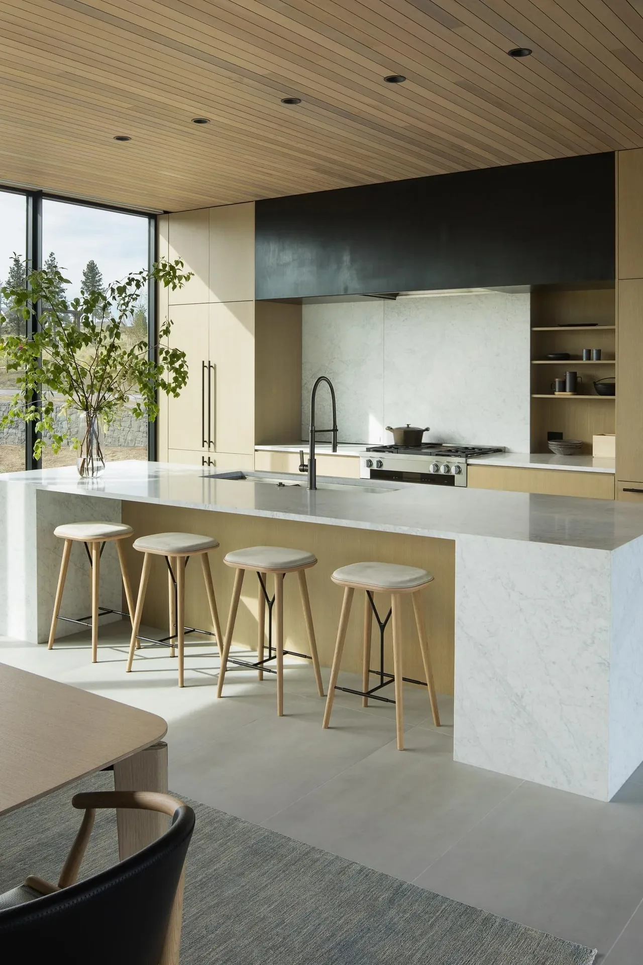 Kitchen features a marble island with wood base, wood-paneled ceiling, and black faucet over undermount sink.