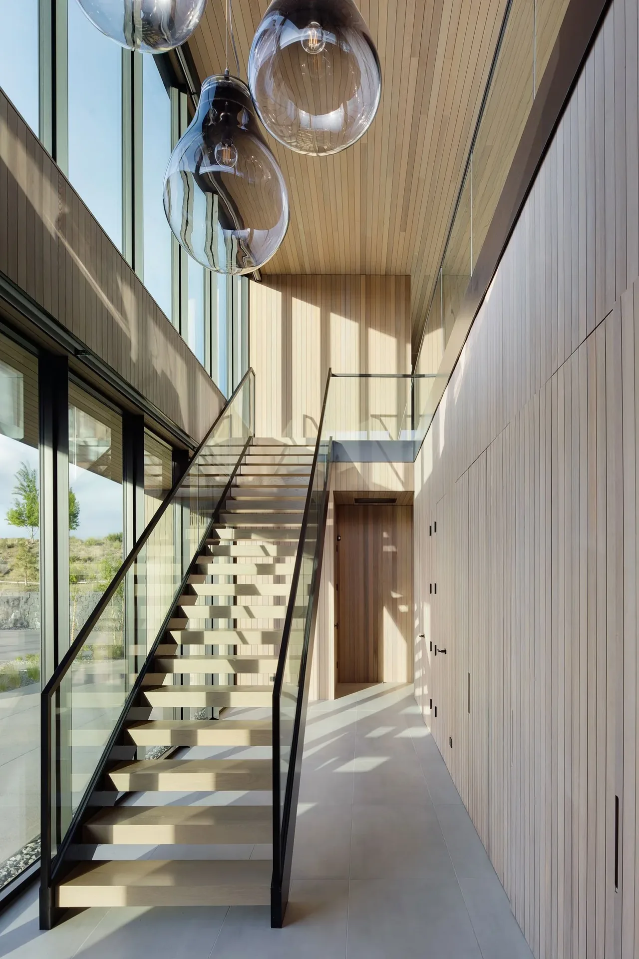 The Expanse showcases a floating staircase with glass railings and continuous wood paneling in a bright, two-story entry space.