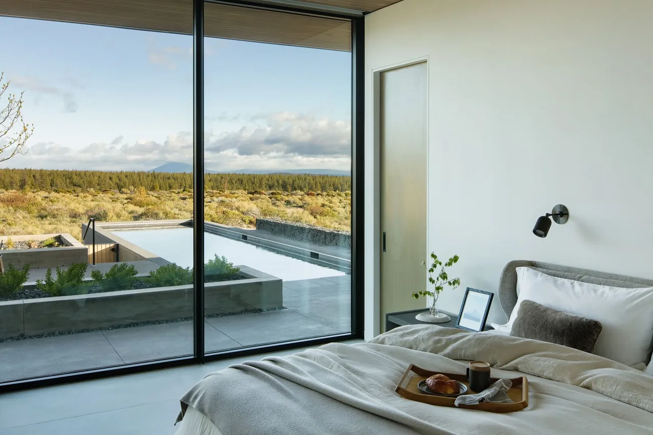 Modern bedroom features a large glass sliding door leading to a pool and scenic outdoor view.