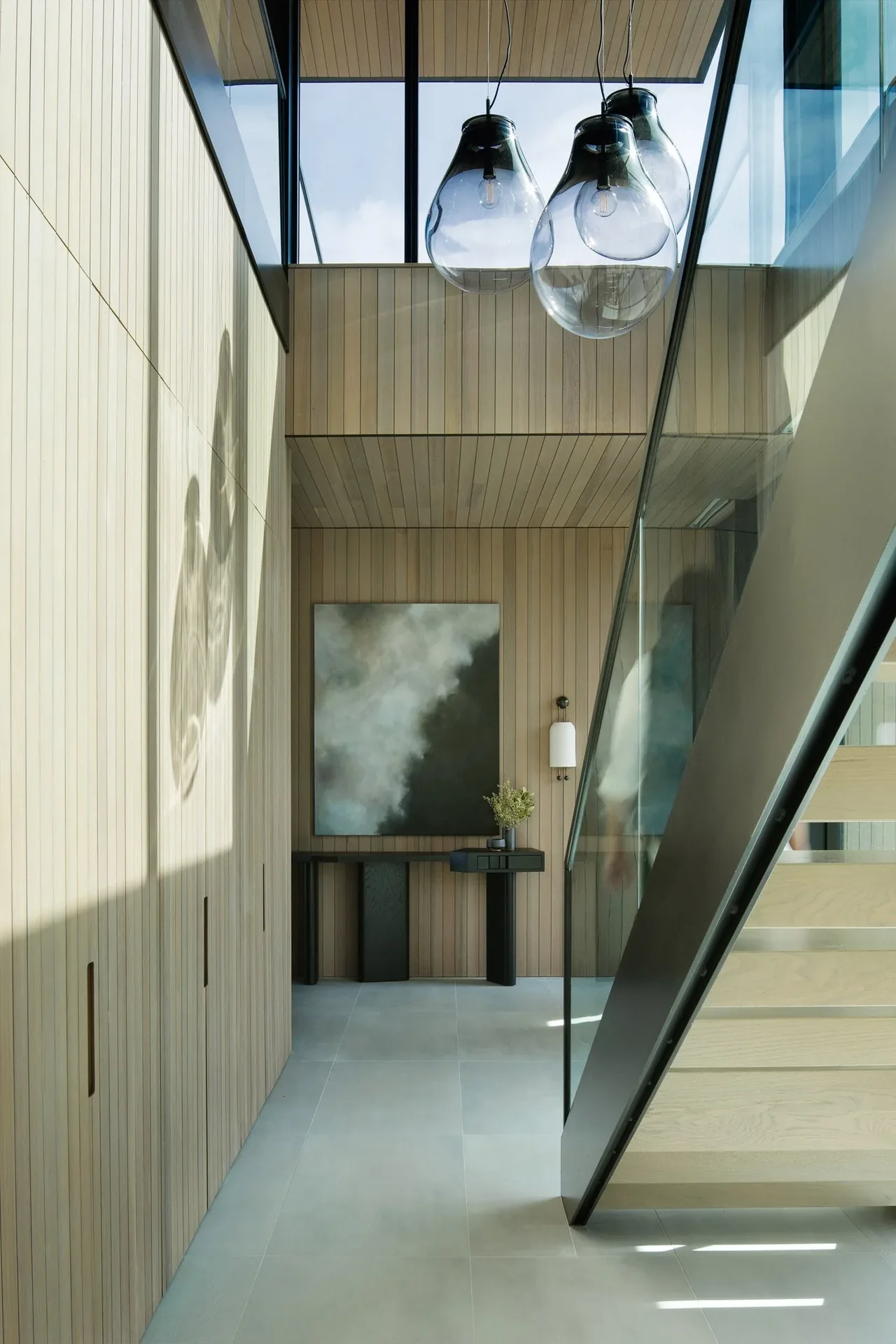 Modern entry space with wood panel walls, glass stair railing, and artistic lighting fixtures.
