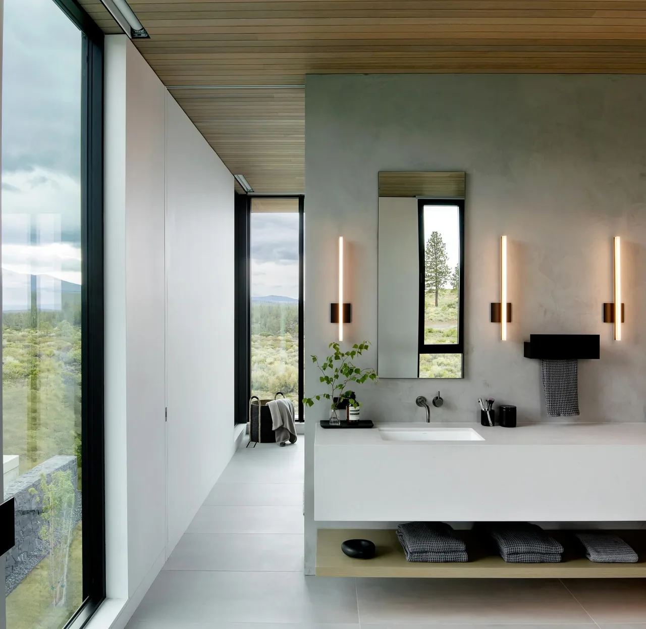 Bathroom with a floating vanity, vertical wall sconces, and large windows offering a scenic landscape view.