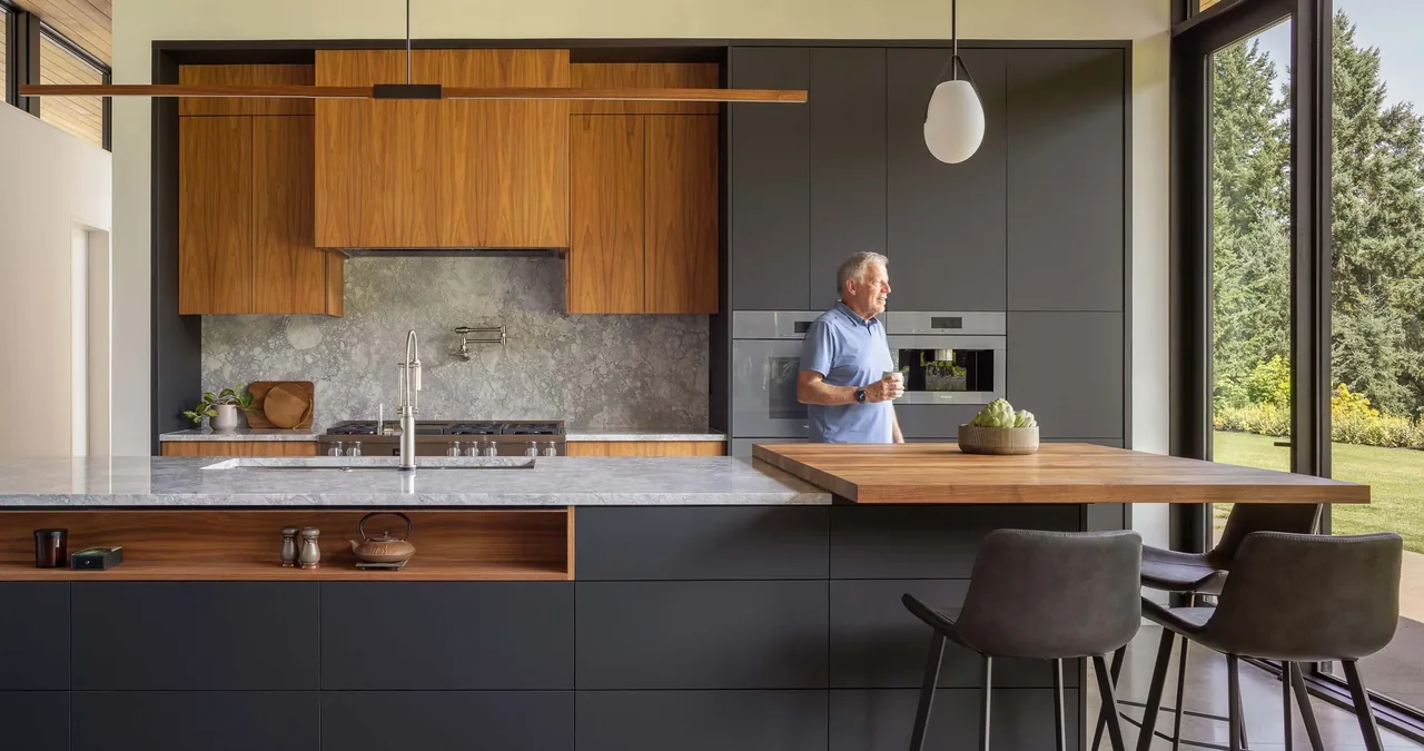 Modern kitchen featuring wood cabinets, stone countertops, and large corner glass windows with a view of the outdoors.