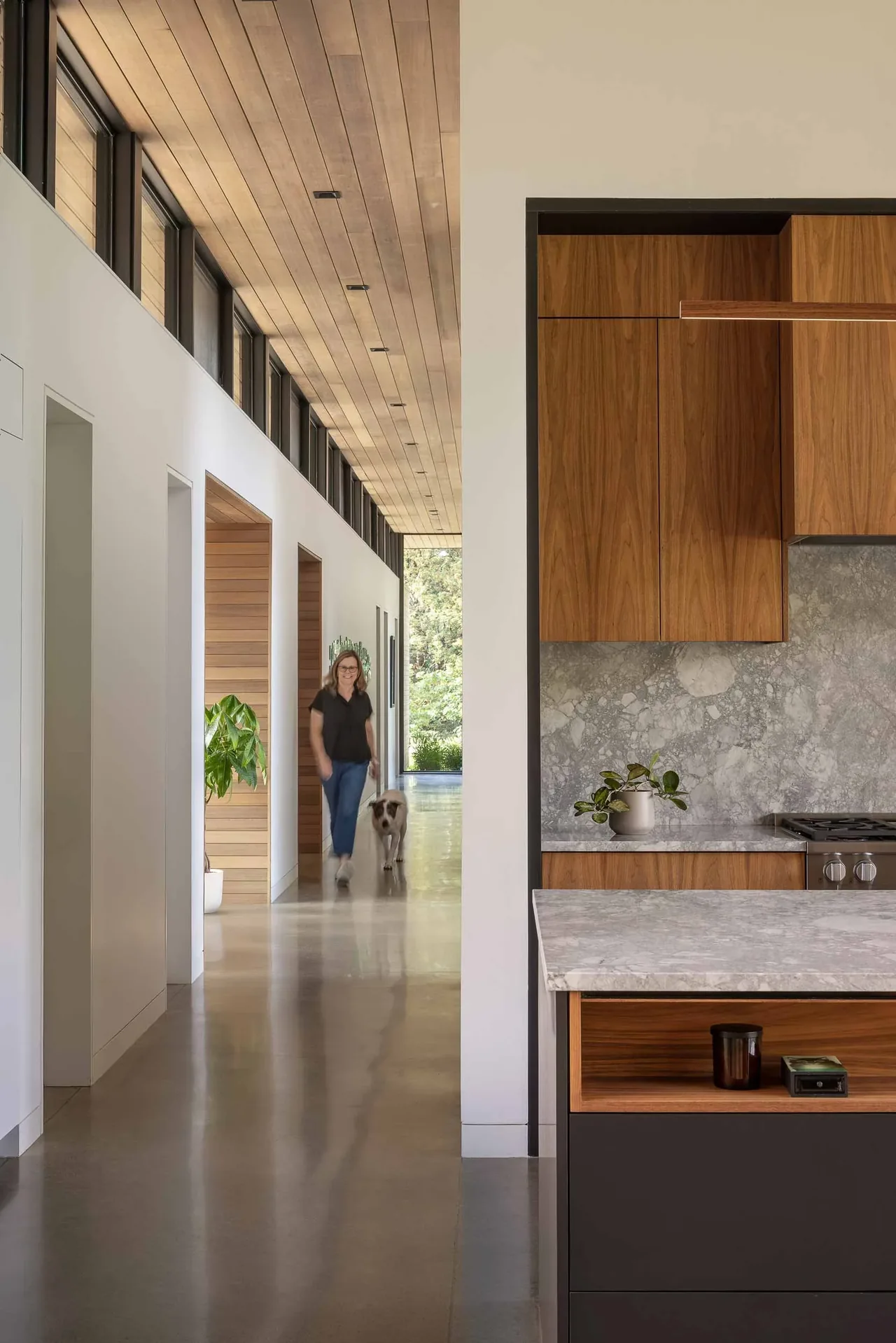 Interior hallway with clerestory windows and wood ceiling next to kitchen featuring wood cabinets and marble countertop.