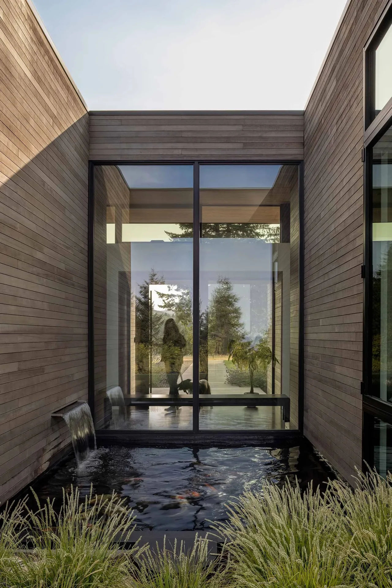 A wood-sided courtyard features a pond with a waterfall and large glass windows reflecting trees outside.