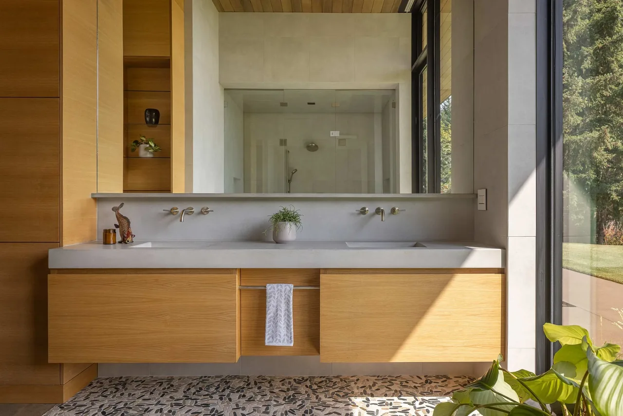 Modern bathroom with floating wood vanity, terrazzo floor, and floor-to-ceiling window with natural light.