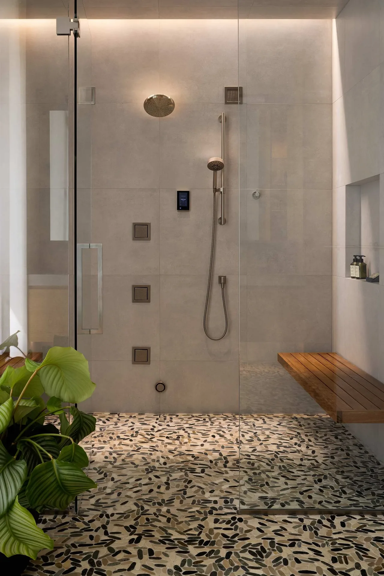 Walk-in shower features pebble stone flooring, a mounted wood bench, and a glass door in a modern bathroom design.
