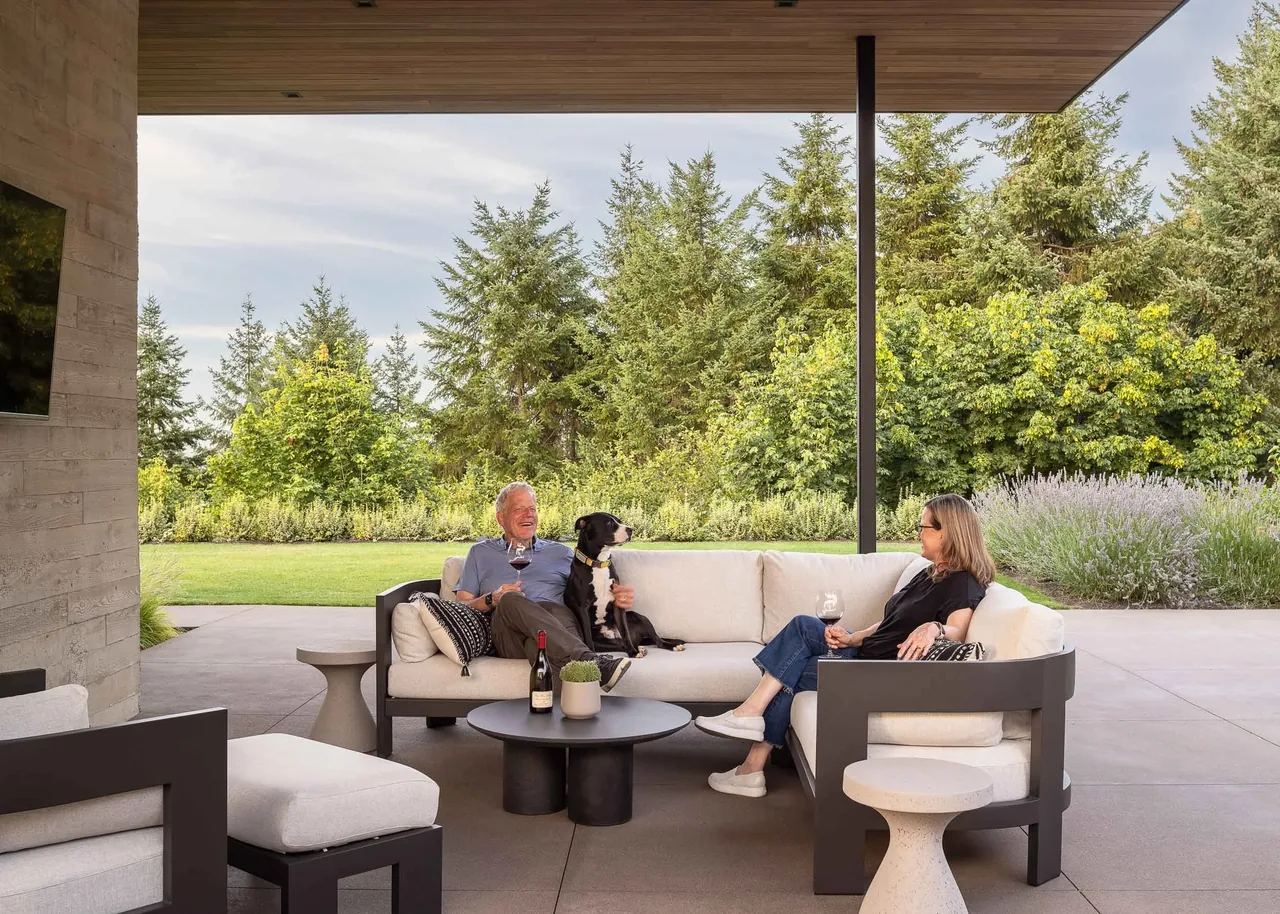 Outdoor covered patio seating area with modern furniture and a view of landscaped greenery and trees.