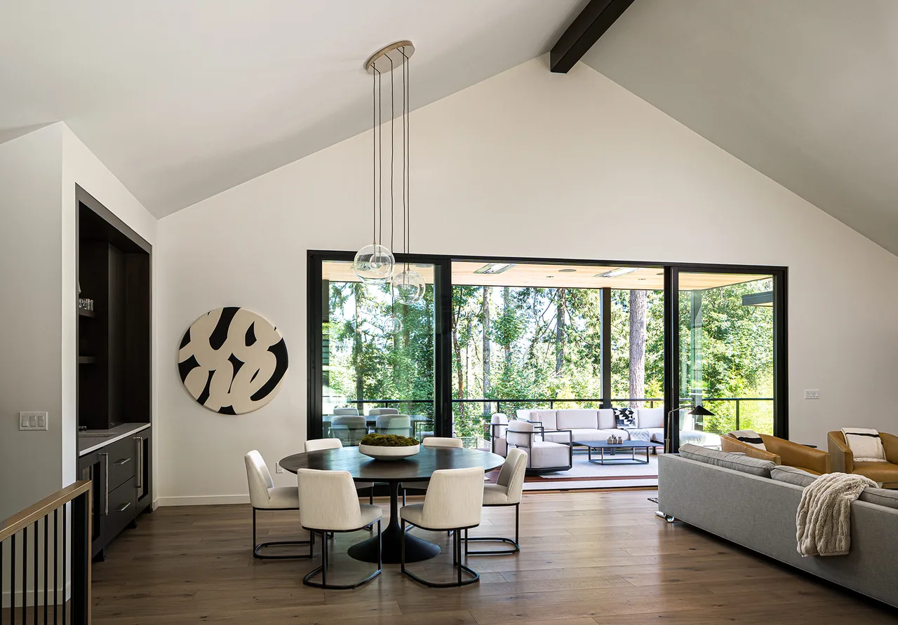 Dining area with vaulted ceiling adjacent to living room and covered outdoor seating area visible through large sliding glass doors.