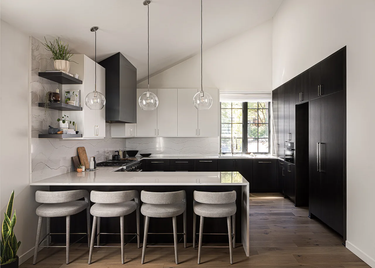 Modern kitchen with black and white cabinetry, marble-look countertops, round glass globe pendants, and gray cushioned bar stools.