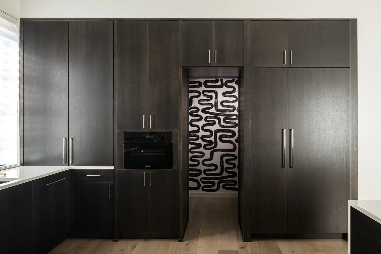 Kitchen cabinetry in dark wood with integrated oven and a doorway to a pantry featuring abstract black and white wall art.