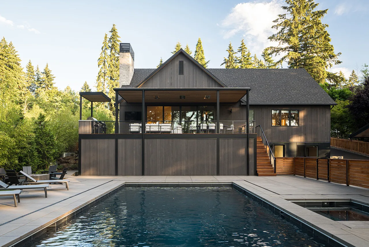 Fernwood House rear view with black stained vertical wood siding, steep roof, covered deck, and pool, designed by Giulietti Schouten Weber Architects.