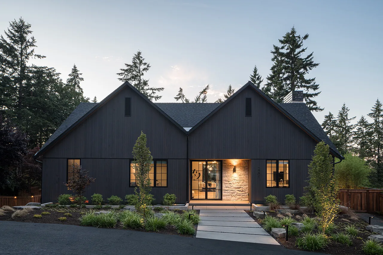 Fernwood House features dark vertical wood siding, steep gable roofs, and black window frames in a wooded setting.