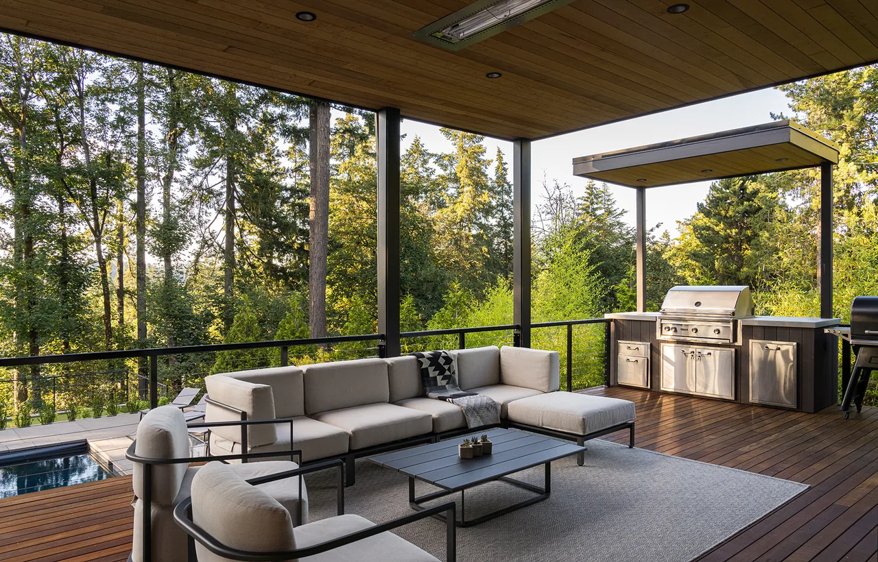 Outdoor living deck with seating and a covered built-in grill area overlooking trees.