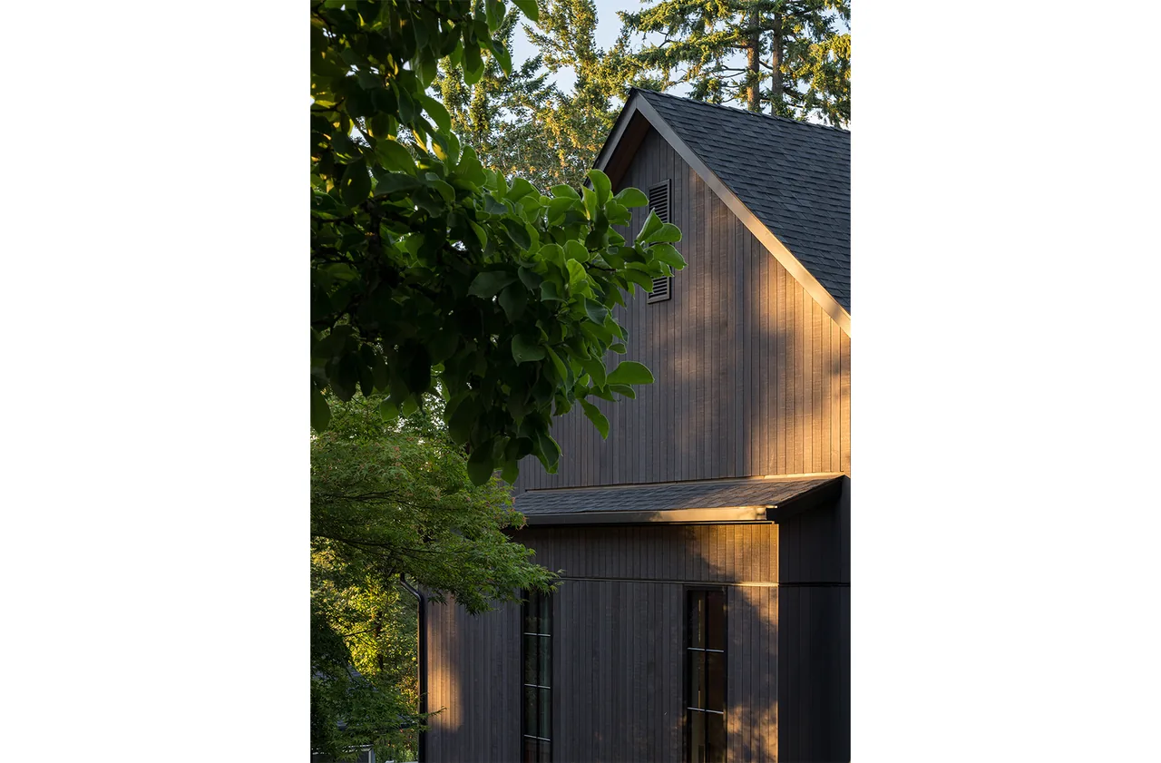 Fernwood House exterior showing vertical wood siding and a steep gable roof during sunlight and shadows.