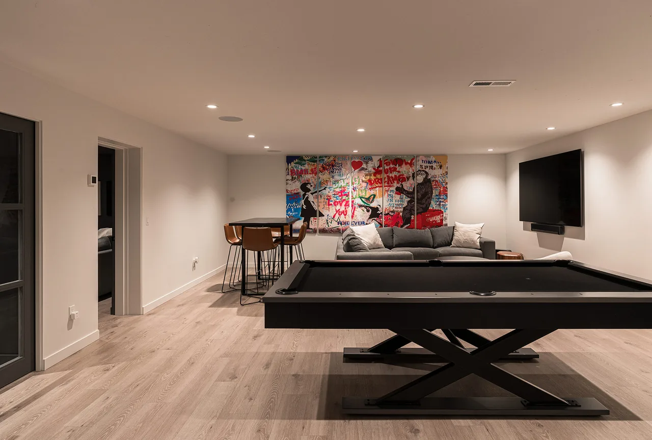 Game room featuring a black pool table, gray sofa, abstract wall art, and a mounted flat screen TV.