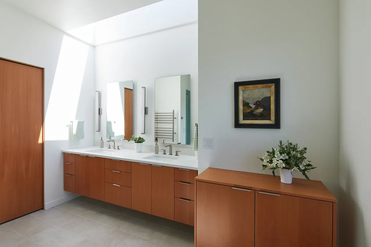Bathroom featuring a floating double vanity with wooden cabinetry and two mirrors, illuminated by natural light from a clerestory window.