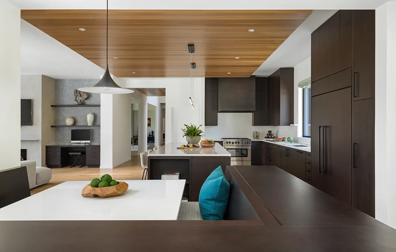The Hilltop House kitchen features dark wood cabinets, a white island, and a wood-paneled ceiling above the dining area.